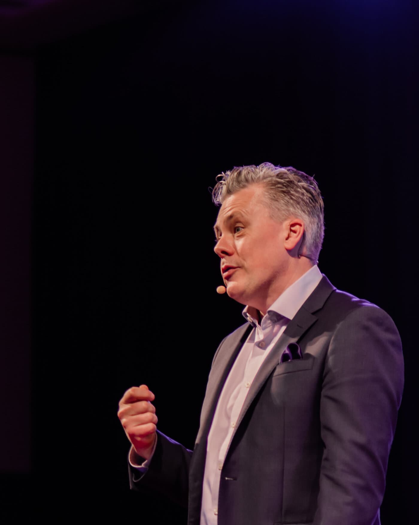 Mark Jones CSP mid-keynote in a spotlight, headset mic, addressing a darkened room