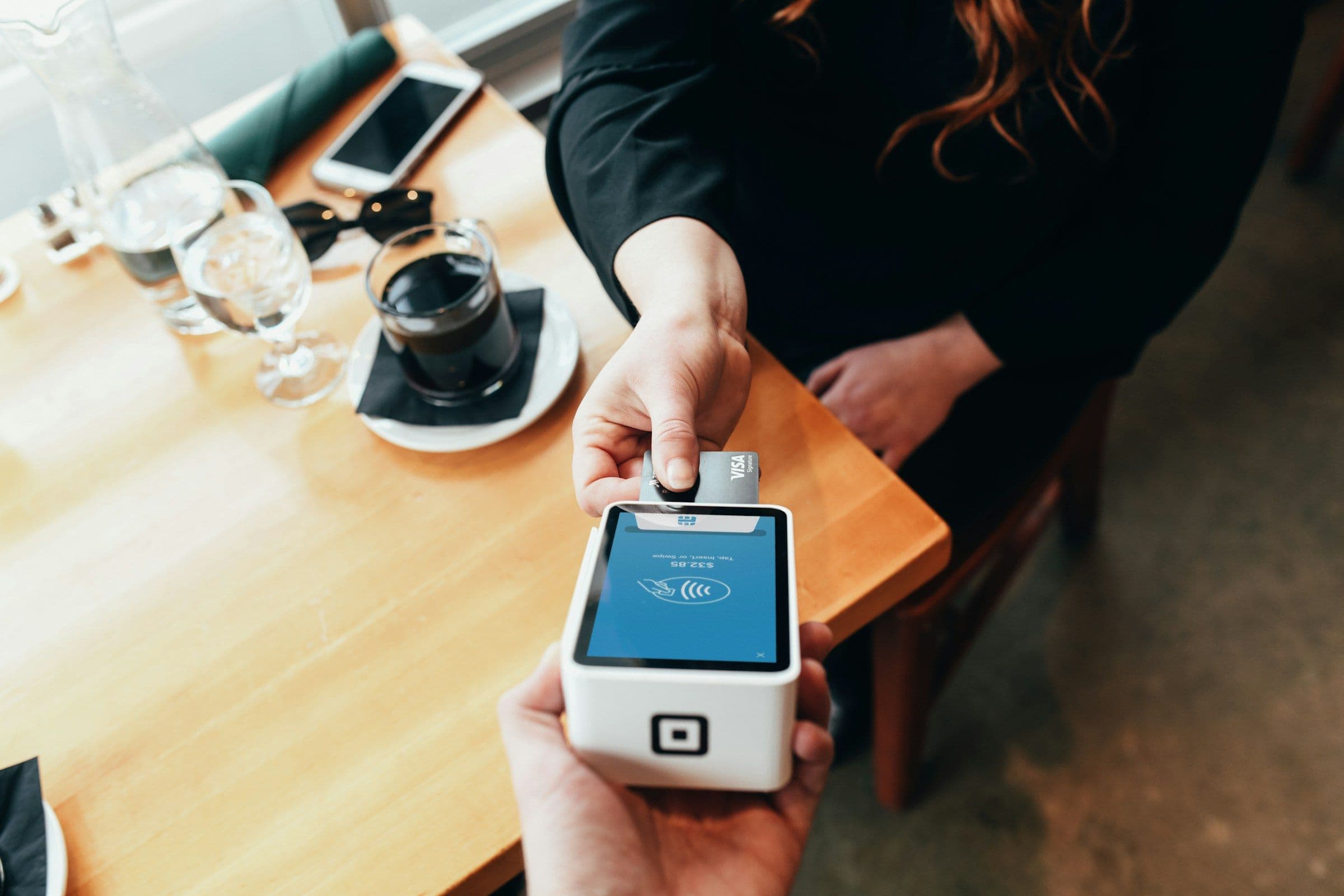 A hand tapping a bank card on a payment terminal at a cafe table